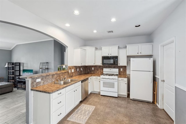 kitchen with sink, white appliances, dark stone countertops, white cabinets, and kitchen peninsula