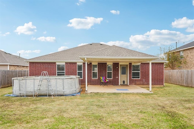 rear view of property featuring a fenced in pool, a patio, and a lawn