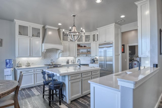 kitchen with white cabinets, custom range hood, an island with sink, and stainless steel built in refrigerator