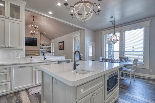 kitchen featuring a kitchen island with sink, stainless steel microwave, vaulted ceiling, and sink