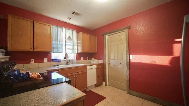 kitchen with a textured ceiling, sink, light tile patterned floors, dishwasher, and hanging light fixtures