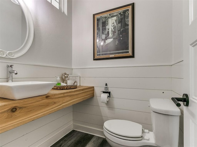 bathroom with wooden walls, sink, wood-type flooring, and toilet