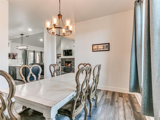 dining area with lofted ceiling, a stone fireplace, sink, dark hardwood / wood-style floors, and a chandelier