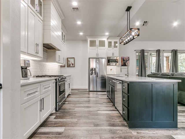 kitchen featuring white cabinets, hanging light fixtures, custom range hood, wood-type flooring, and stainless steel appliances