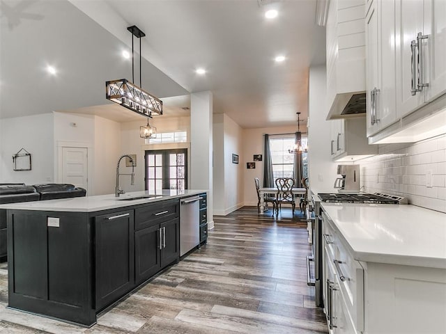 kitchen with stainless steel appliances, white cabinetry, hanging light fixtures, and an island with sink