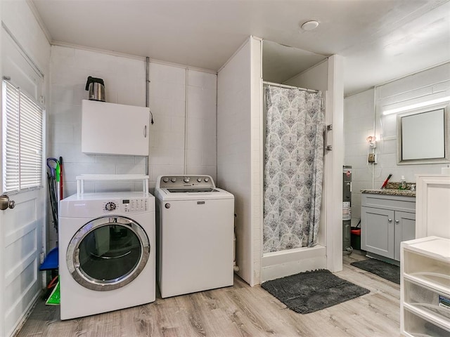 laundry room with water heater, light wood-type flooring, tile walls, and separate washer and dryer