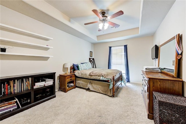 carpeted bedroom with ceiling fan and a tray ceiling