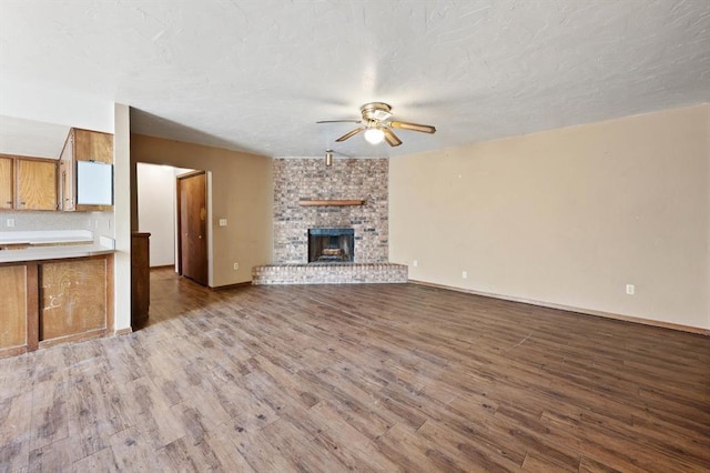 unfurnished living room with ceiling fan, a large fireplace, wood-type flooring, and a textured ceiling