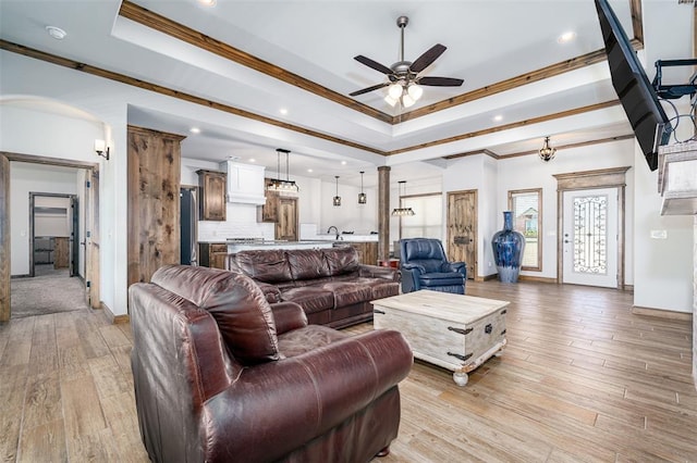 living room with light wood-type flooring, a raised ceiling, ceiling fan, and crown molding