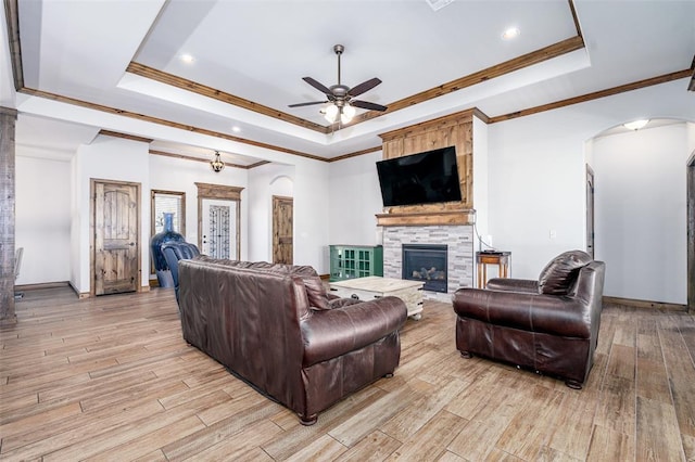 living room with crown molding, light hardwood / wood-style floors, a raised ceiling, and a fireplace