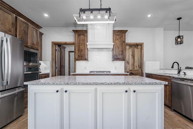 kitchen with white cabinets, decorative light fixtures, a kitchen island, and stainless steel appliances