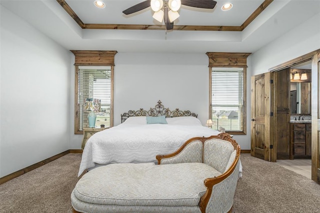 carpeted bedroom with a tray ceiling, ensuite bath, ceiling fan, and ornamental molding