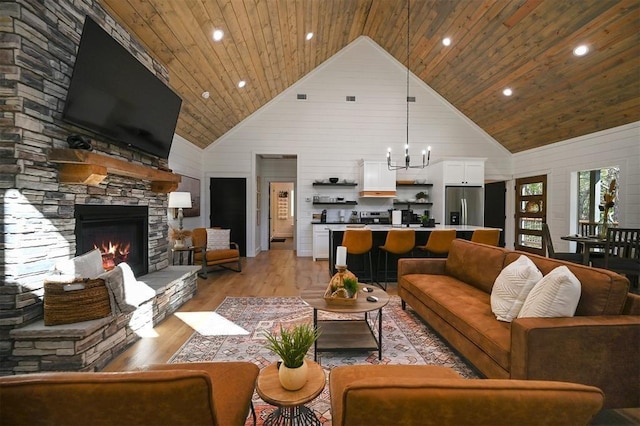 living room featuring a chandelier, light wood-type flooring, high vaulted ceiling, and a stone fireplace