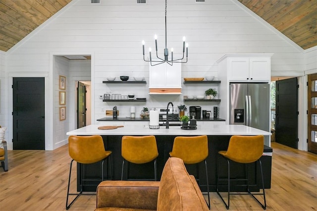 kitchen featuring a kitchen bar, stainless steel refrigerator with ice dispenser, light wood-type flooring, white cabinets, and hanging light fixtures