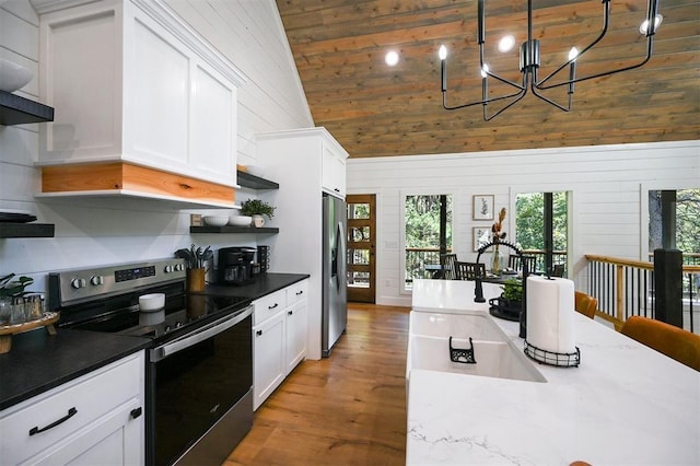 kitchen with white cabinetry, hanging light fixtures, light hardwood / wood-style flooring, wooden walls, and appliances with stainless steel finishes