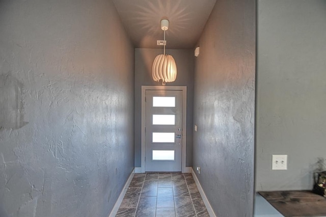 doorway with a textured wall and baseboards