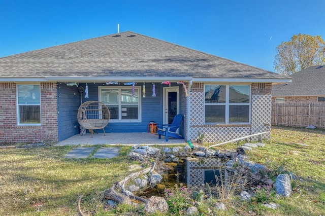 rear view of property with a shingled roof, a patio area, a yard, and fence