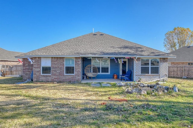 back of house featuring roof with shingles, a lawn, a patio area, and fence