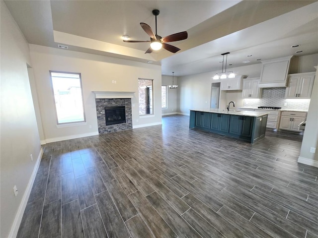 kitchen featuring dark wood-type flooring, a kitchen island with sink, custom range hood, white cabinets, and ceiling fan with notable chandelier