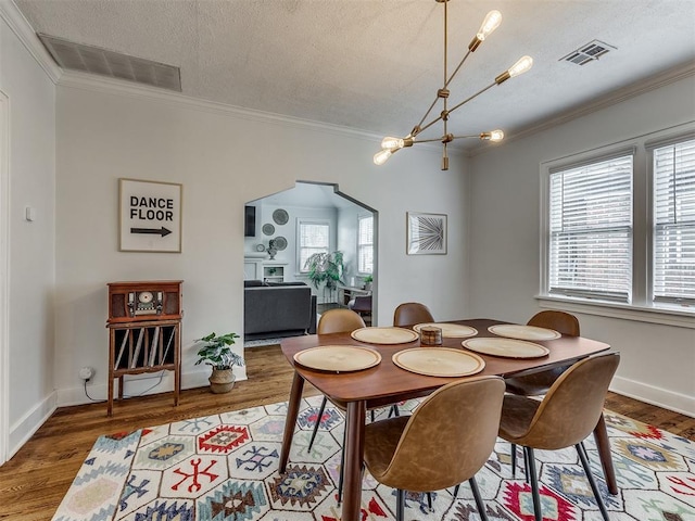 dining space with hardwood / wood-style floors, a textured ceiling, crown molding, and a healthy amount of sunlight