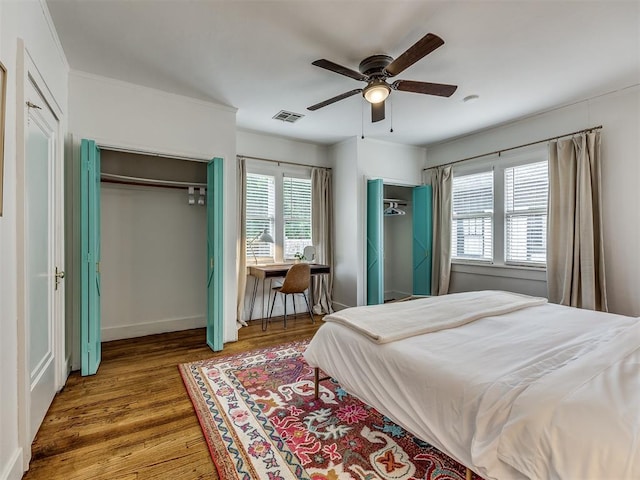 bedroom with hardwood / wood-style floors, ceiling fan, and multiple closets