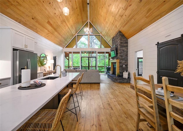 dining space featuring sink, a barn door, high vaulted ceiling, a notable chandelier, and light hardwood / wood-style floors