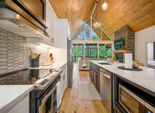 kitchen with wall chimney exhaust hood, stainless steel appliances, pendant lighting, light hardwood / wood-style flooring, and white cabinets