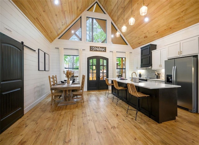 kitchen with a barn door, high vaulted ceiling, stainless steel fridge with ice dispenser, hanging light fixtures, and an island with sink