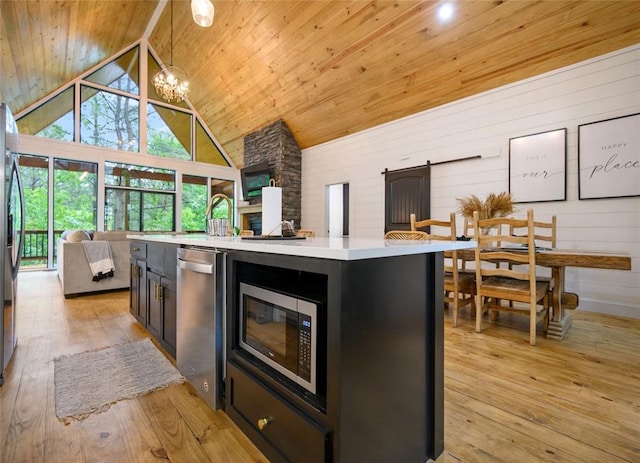 kitchen featuring appliances with stainless steel finishes, pendant lighting, a barn door, a center island, and light hardwood / wood-style floors