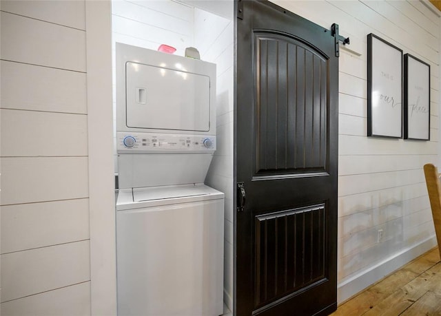 laundry area with stacked washer / drying machine, a barn door, and light hardwood / wood-style floors