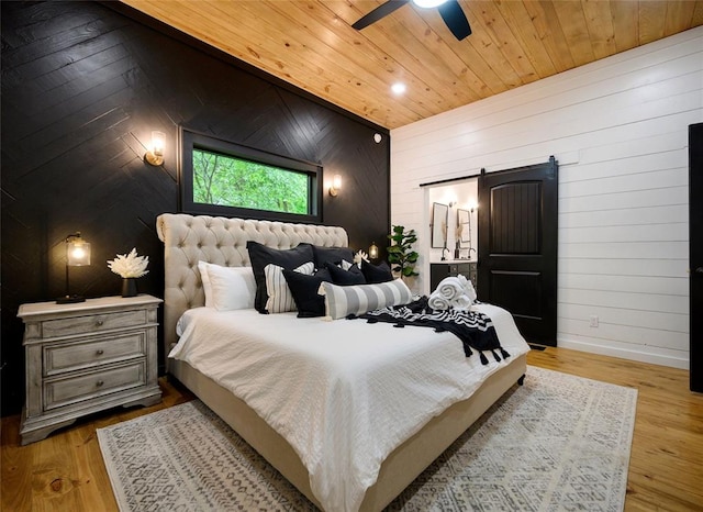 bedroom with light wood-type flooring, a barn door, ceiling fan, and wood walls