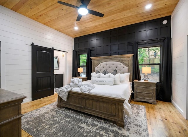 bedroom featuring wood walls, wooden ceiling, ceiling fan, a barn door, and light wood-type flooring