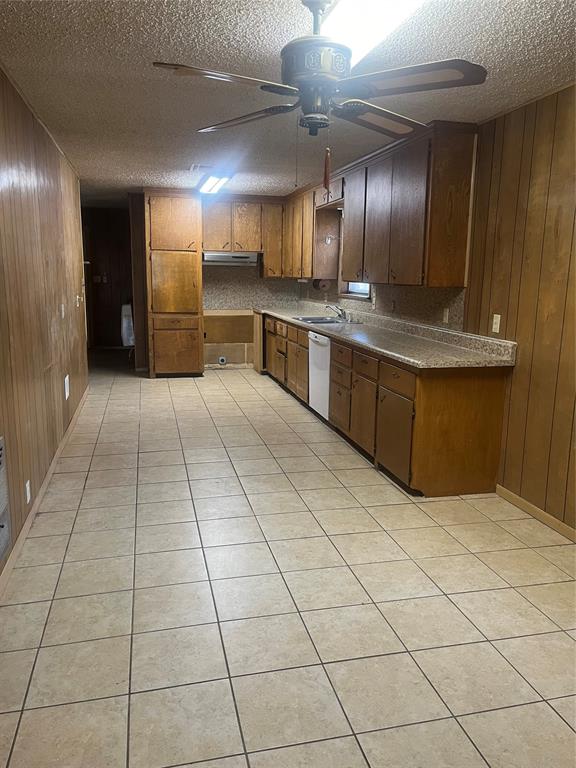 kitchen with dishwasher, a textured ceiling, and wooden walls