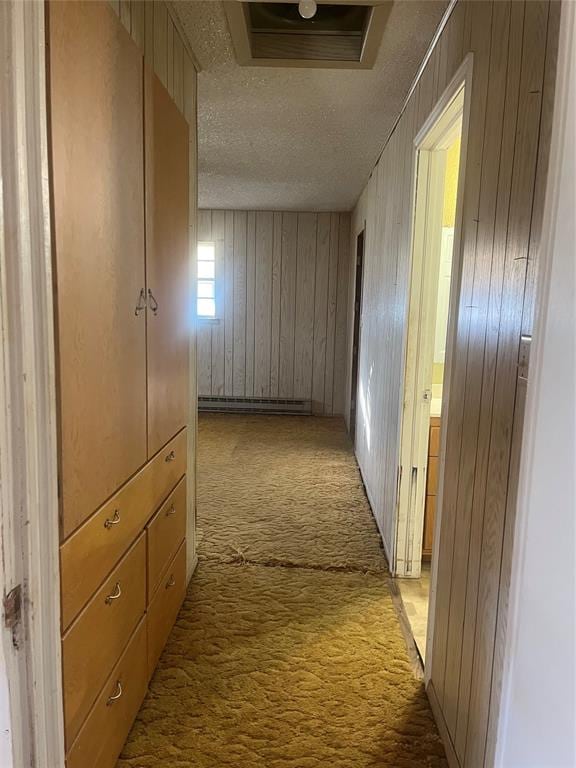 corridor featuring light colored carpet, baseboard heating, a textured ceiling, and wooden walls