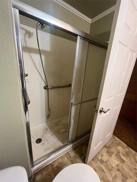 bathroom with toilet, crown molding, and a shower with shower door