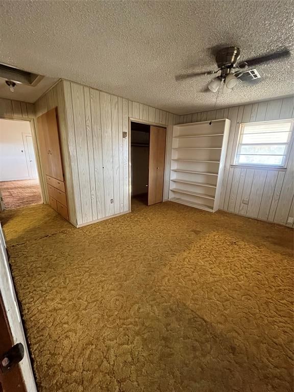 unfurnished bedroom with carpet floors, wood walls, ceiling fan, and a textured ceiling