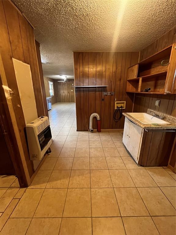 kitchen with a textured ceiling, heating unit, sink, light tile patterned floors, and wood walls