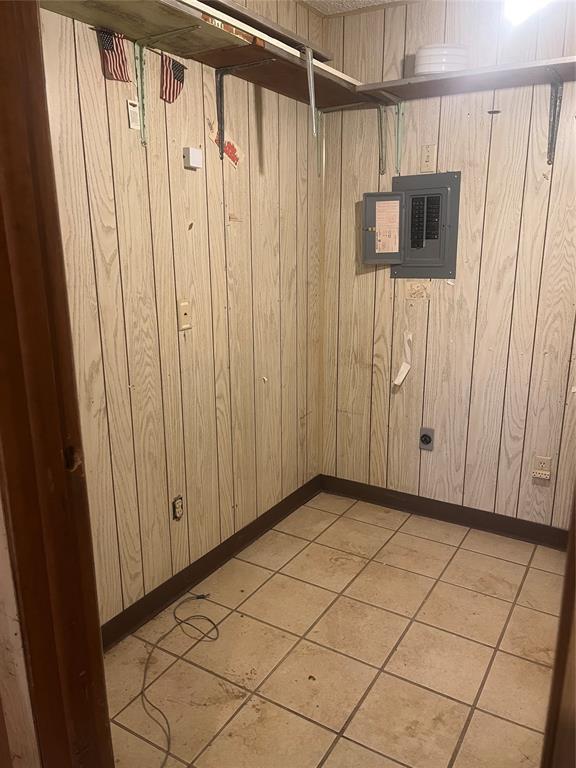 basement featuring electric panel, wooden walls, and light tile patterned flooring