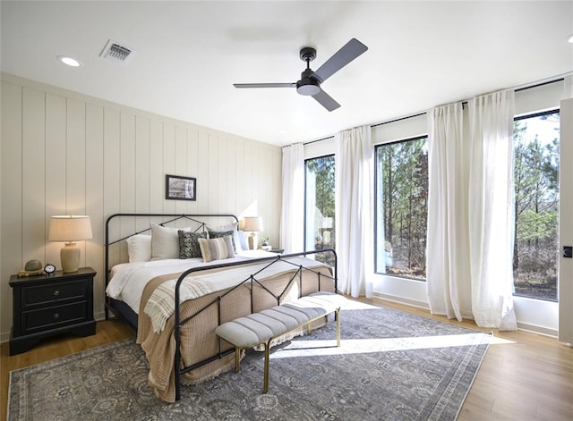 bedroom with ceiling fan, wooden walls, and dark wood-type flooring