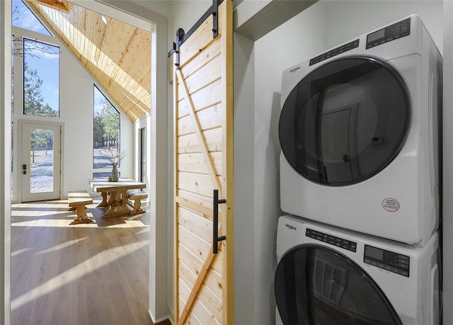 washroom with a barn door, stacked washer and clothes dryer, and hardwood / wood-style flooring