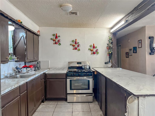 kitchen with sink, stainless steel range with gas cooktop, a textured ceiling, dark brown cabinets, and light tile patterned floors