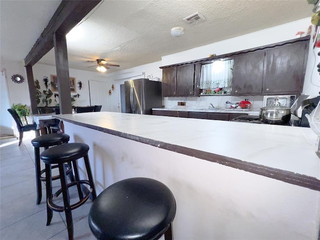 kitchen featuring a textured ceiling, kitchen peninsula, a breakfast bar area, and stainless steel refrigerator