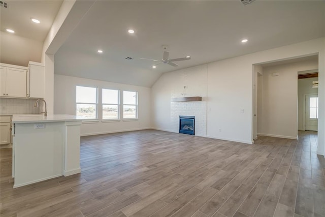 unfurnished living room with ceiling fan, a fireplace, lofted ceiling, and light hardwood / wood-style flooring