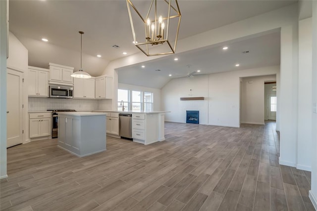 kitchen with decorative light fixtures, white cabinetry, stainless steel appliances, and a brick fireplace