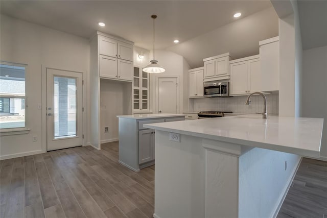 kitchen with kitchen peninsula, vaulted ceiling, sink, decorative light fixtures, and white cabinetry