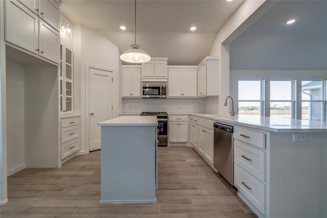 kitchen with white cabinets, hanging light fixtures, tasteful backsplash, kitchen peninsula, and stainless steel appliances