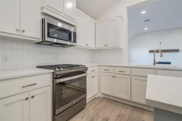 kitchen featuring backsplash, sink, vaulted ceiling, appliances with stainless steel finishes, and white cabinetry