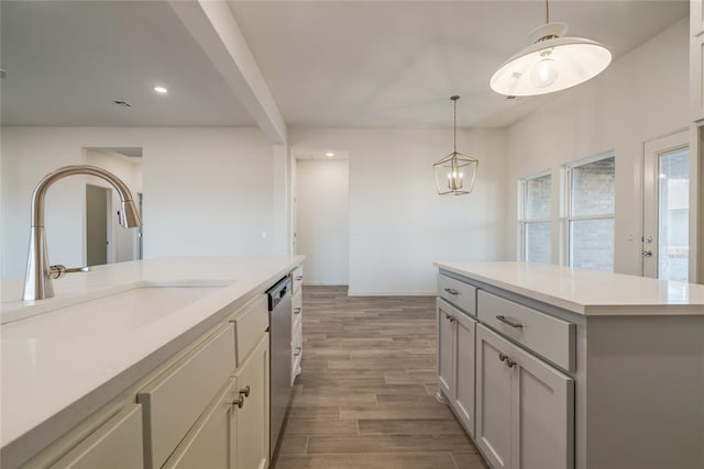 kitchen featuring stainless steel dishwasher, sink, wood-type flooring, decorative light fixtures, and a kitchen island