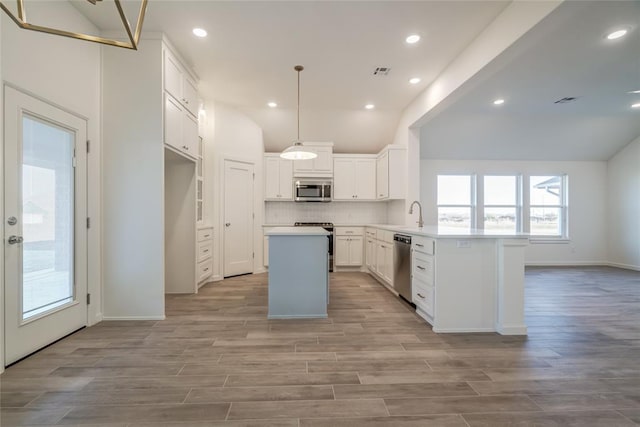 kitchen with appliances with stainless steel finishes, a kitchen island, pendant lighting, white cabinetry, and lofted ceiling