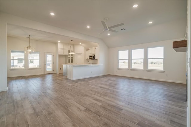 unfurnished living room with light wood-type flooring, ceiling fan with notable chandelier, and lofted ceiling